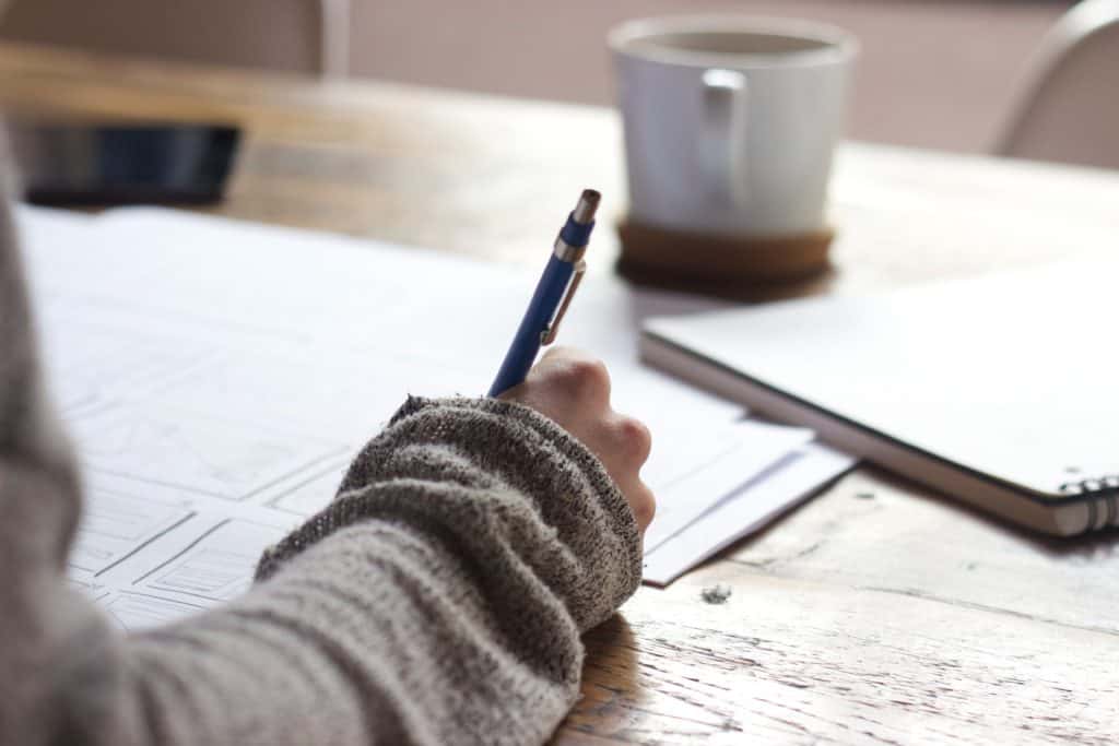 Person writing at a desk with a cup of coffee